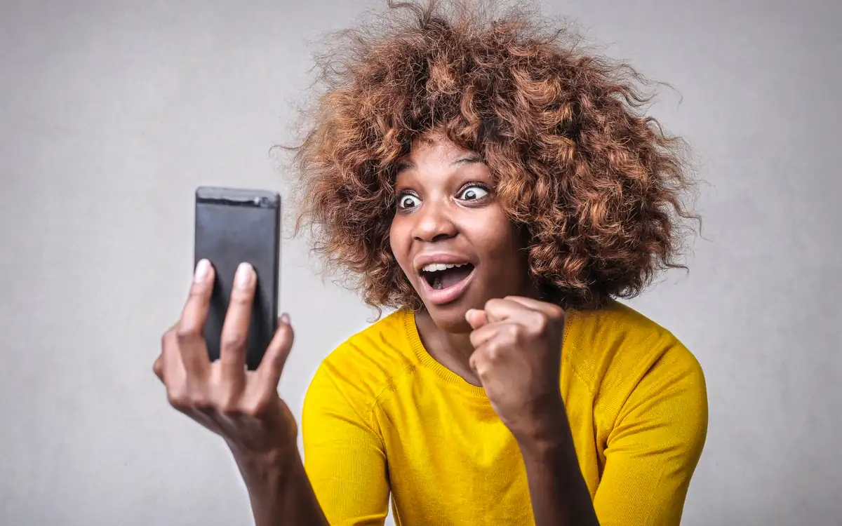Excited woman in yellow reacting to a win on her phone – PHFUN bonus moment